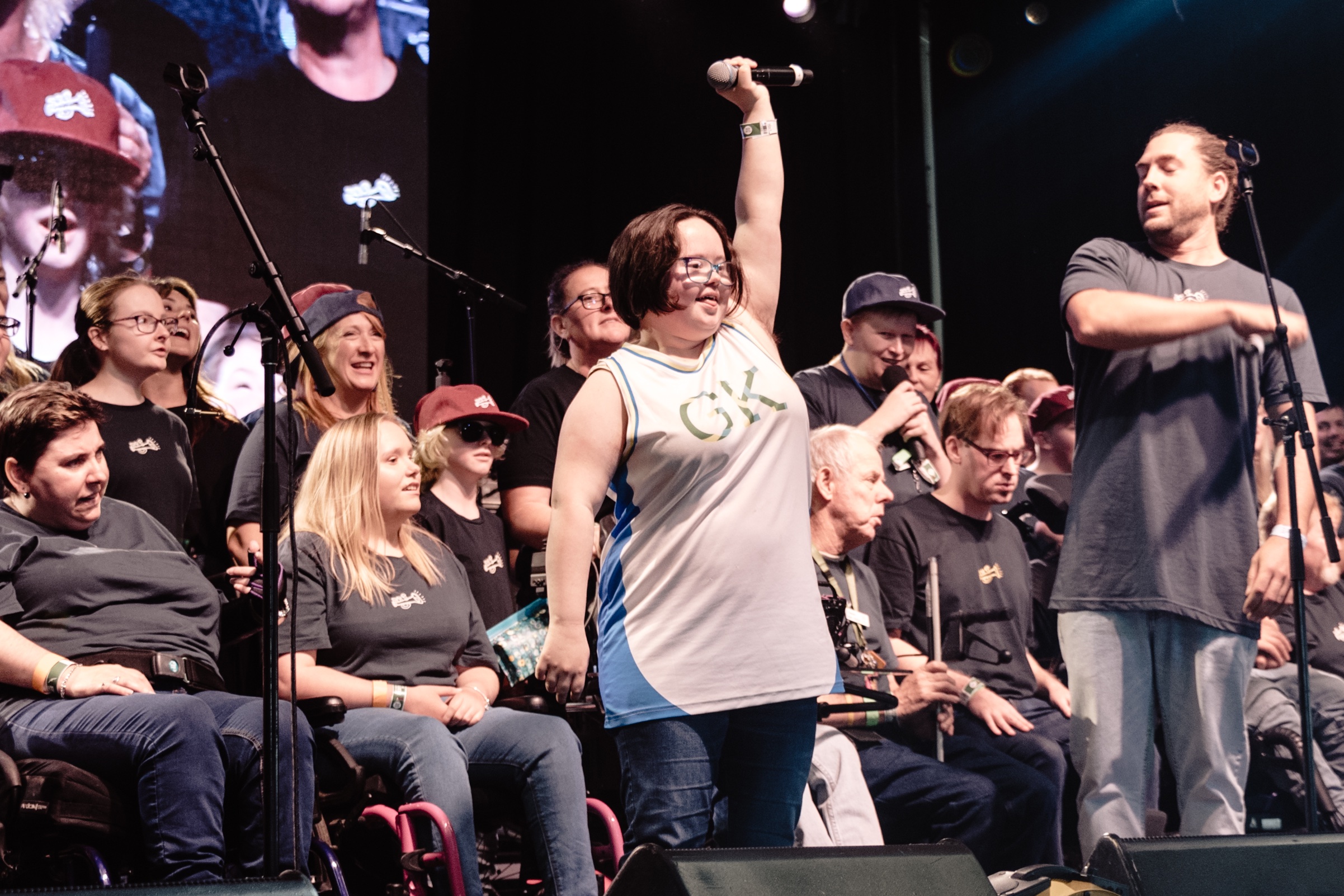 The four members of 19-Twenty stand on a stage with a packed audience behind them. The crowed is cheering and excited.